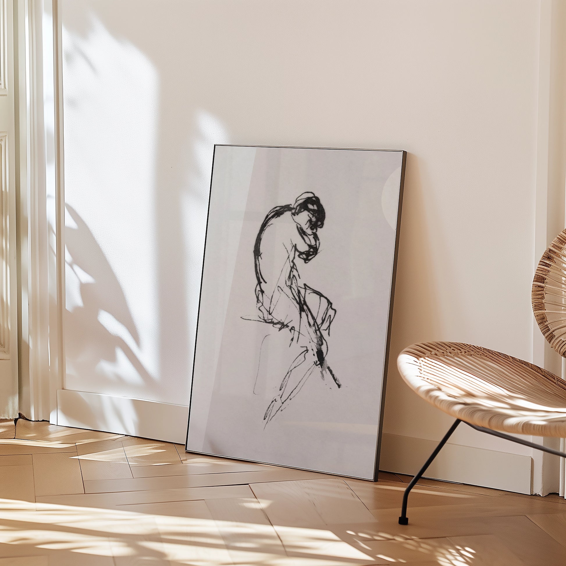 Framed black and white sketch of a seated figure leaning forward, positioned against a light wall in a modern interior setting.