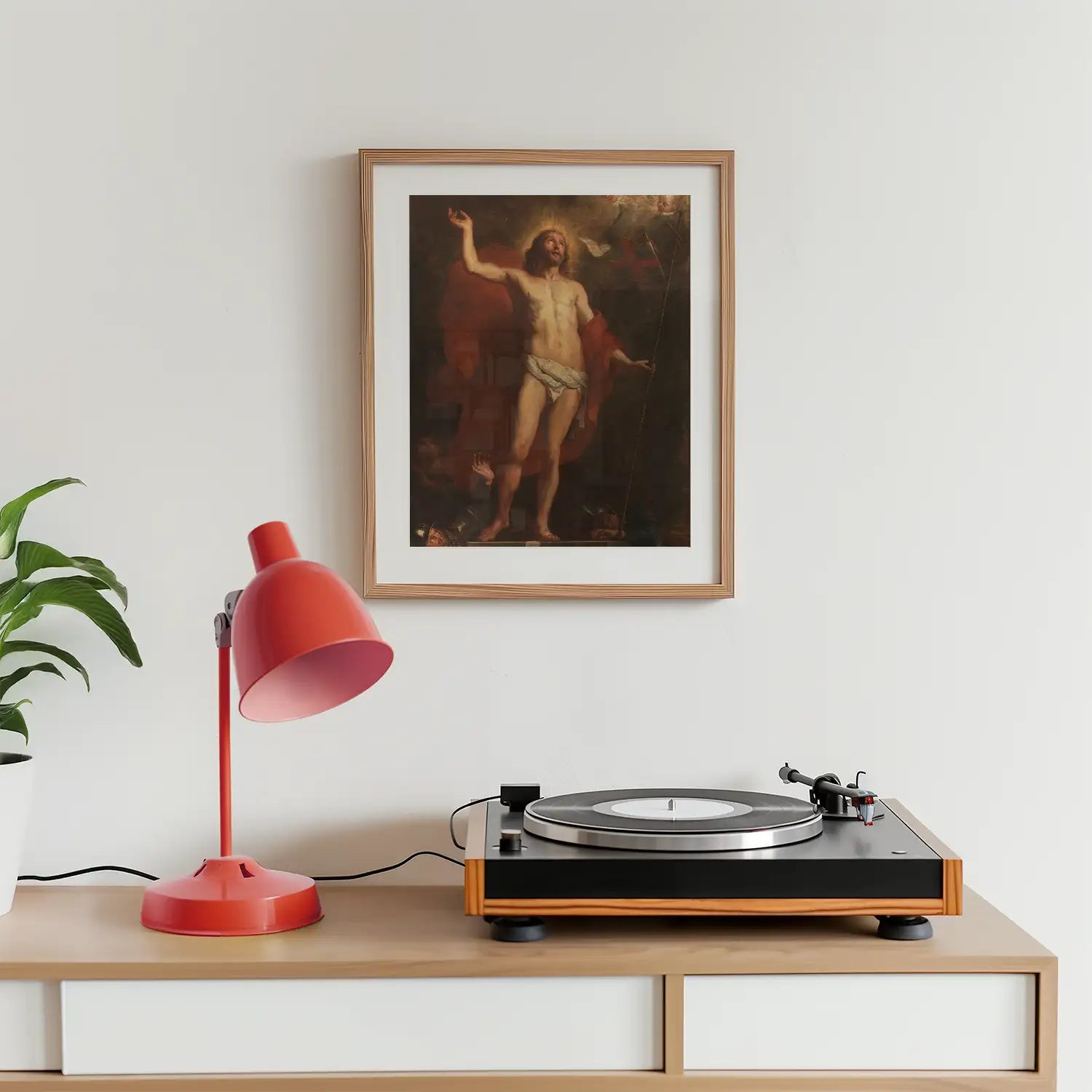 Framed painting of a figure with glowing halo, displayed above a turntable and red desk lamp in a modern interior setting.