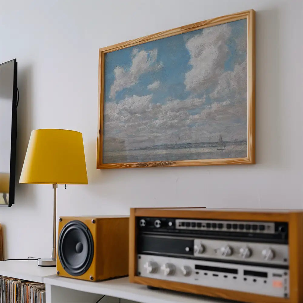 Painting of a serene sky with clouds and a distant sailboat, framed and displayed on a wall above a yellow lamp and vintage audio equipment.