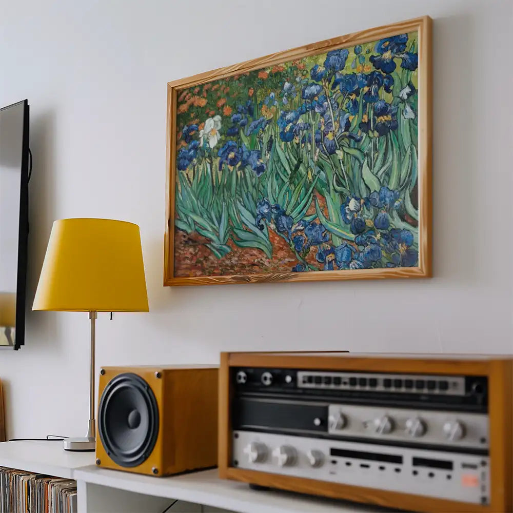 Framed painting of blue irises by Vincent van Gogh displayed on a white wall above a wooden speaker and a yellow lamp.