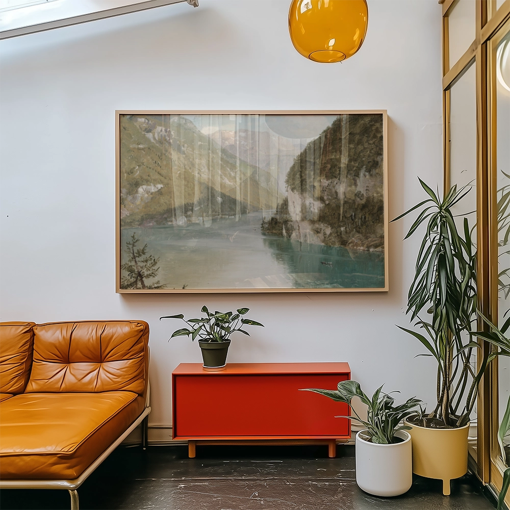 A serene landscape painting featuring a river and mountains, framed and displayed above a stylish orange couch in a modern interior setting with plants and a red cabinet.