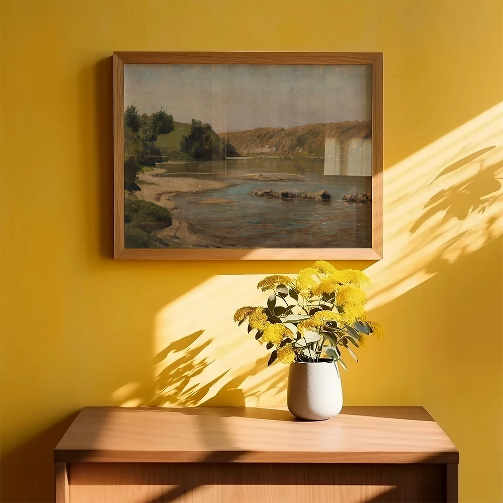 Framed landscape painting on a yellow wall above a wooden table with a vase of yellow flowers.