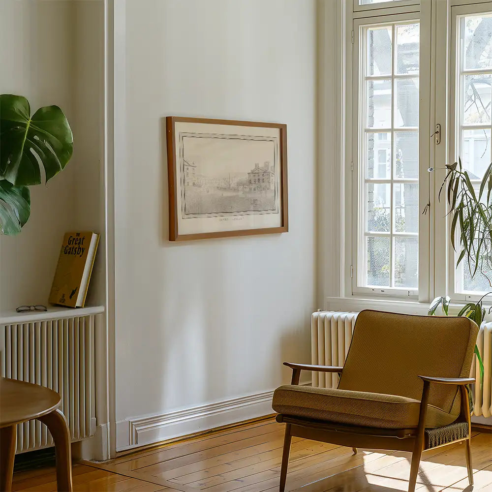 Interior view of a room featuring a framed painting on the wall, a vintage armchair, and a plant, with sunlight filtering through the large windows.