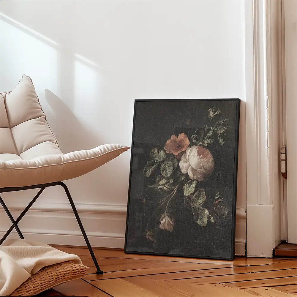 Vintage floral painting in a black frame leaning against a wall beside a modern chair.
