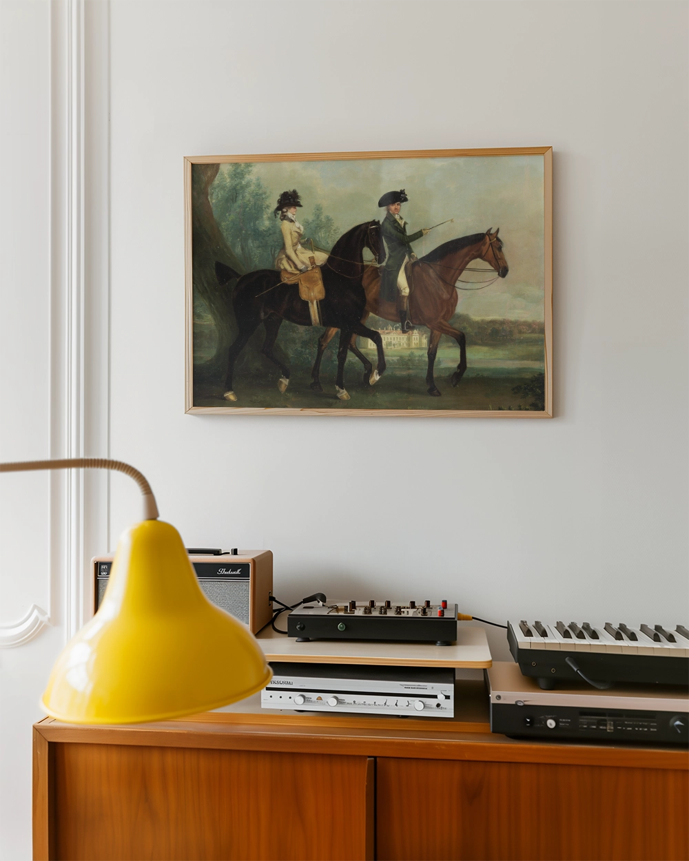 Painting of two riders on horseback set against a serene landscape, displayed in a wooden frame above a vintage console with various audio equipment and a yellow lamp.
