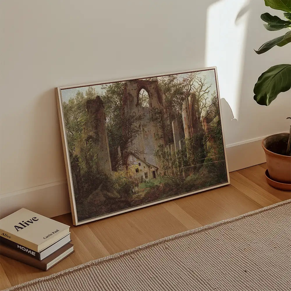 Painting of a ruined castle surrounded by trees, framed and leaning against a wall with books and a potted plant nearby.