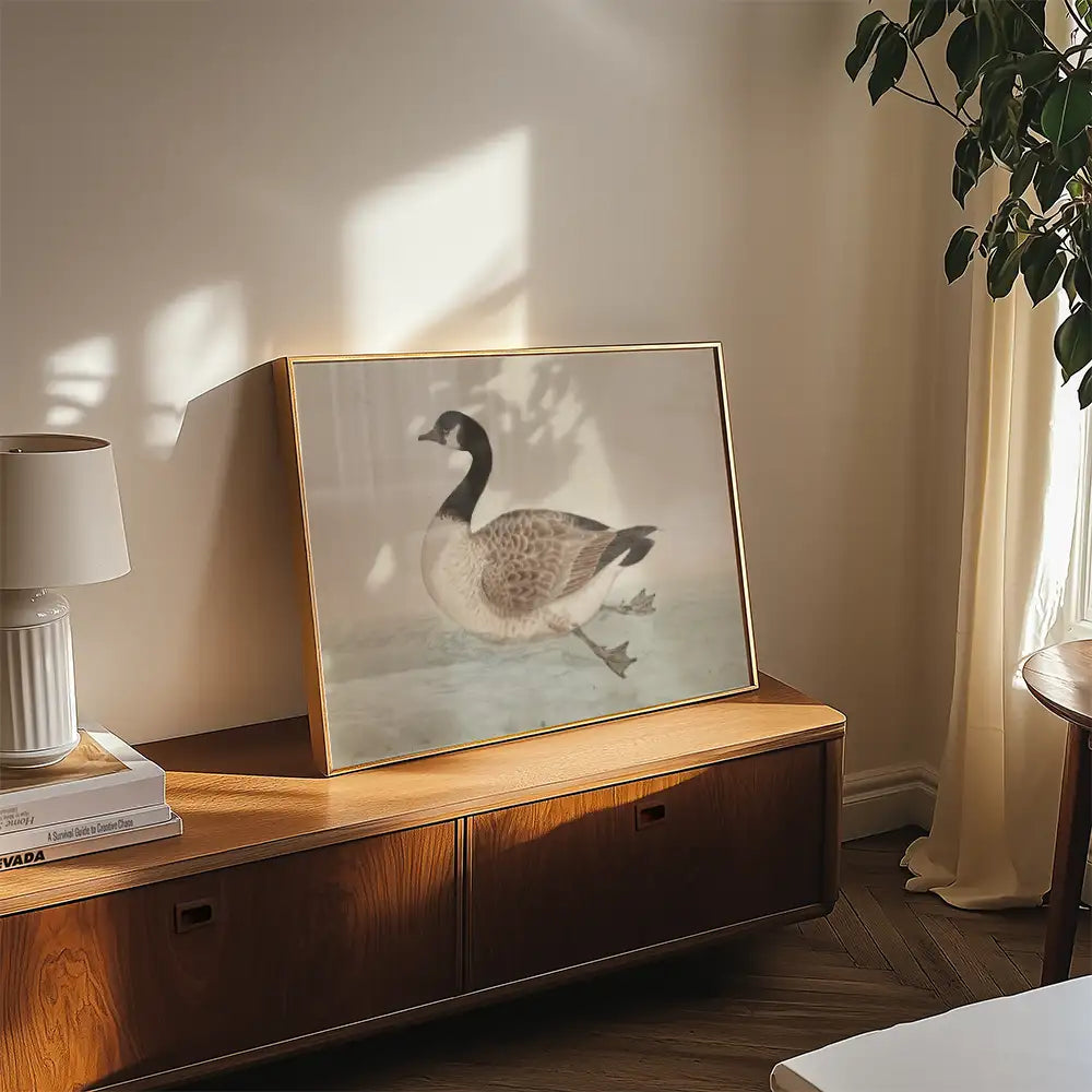 Framed painting of a goose displayed on a wooden side table in a well-lit living room.