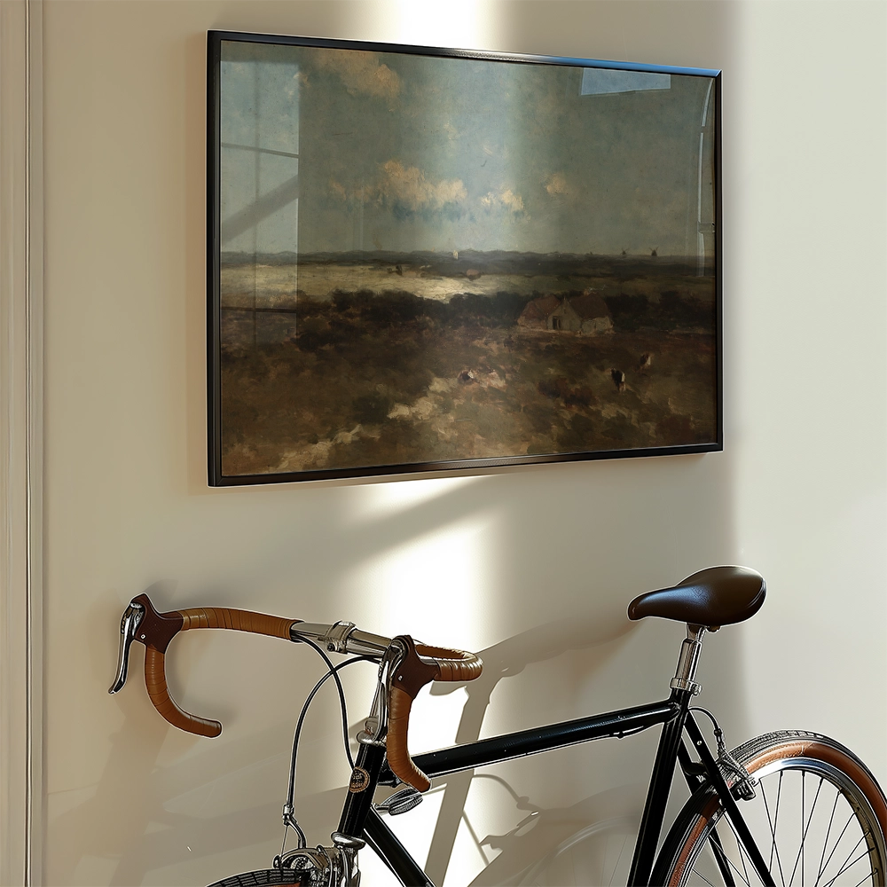Framed landscape painting hanging on a wall next to a black bicycle with brown handlebars.