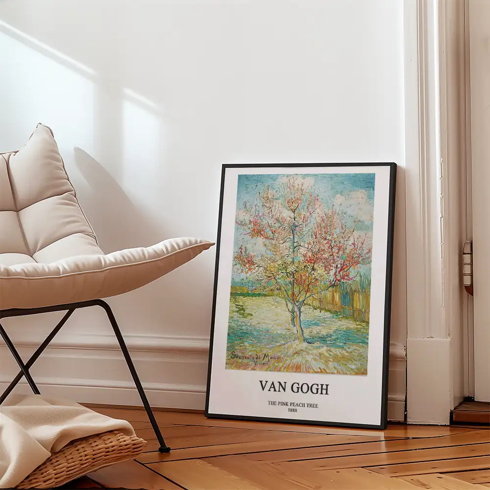 Framed poster of Van Gogh's "The Pink Peach Tree" leaning against a wall next to a stylish chair in a modern interior setting.