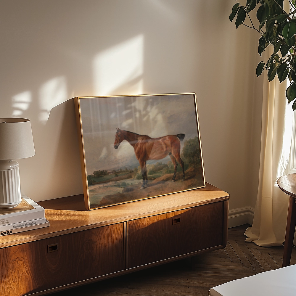 Framed painting of a horse placed on a wooden console table with a lamp and decorative items in a sunlit room.