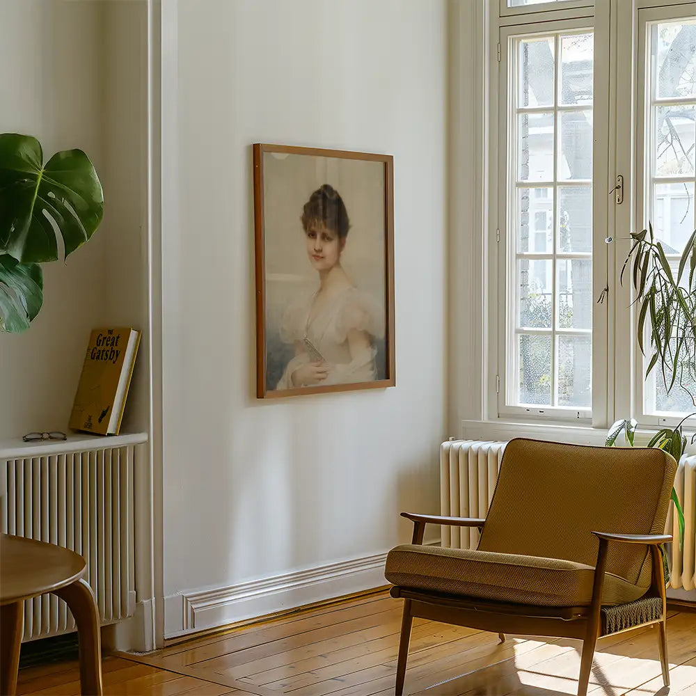 Framed painting of a woman in a soft blue dress displayed on a white wall in a cozy living room with a brown chair and a leafy plant.