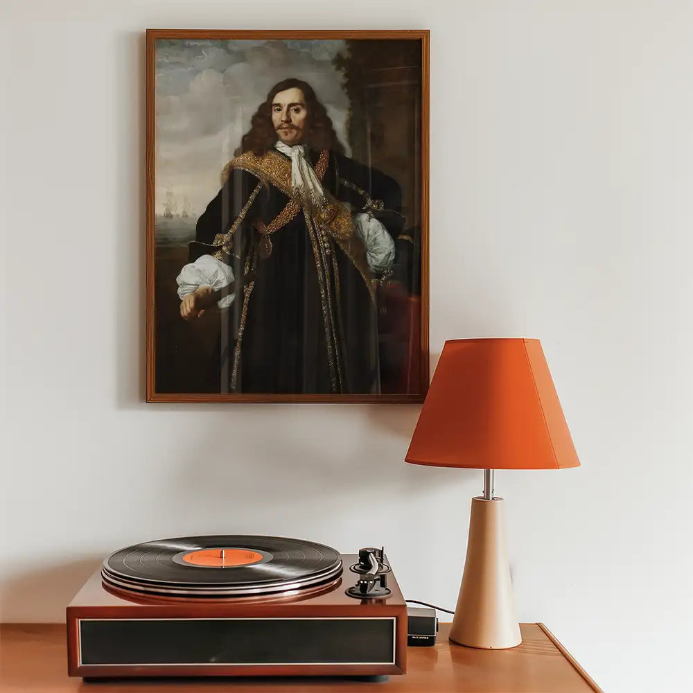 Framed portrait painting of a historical figure hanging on a wall above a wooden record player and an orange bedside lamp.