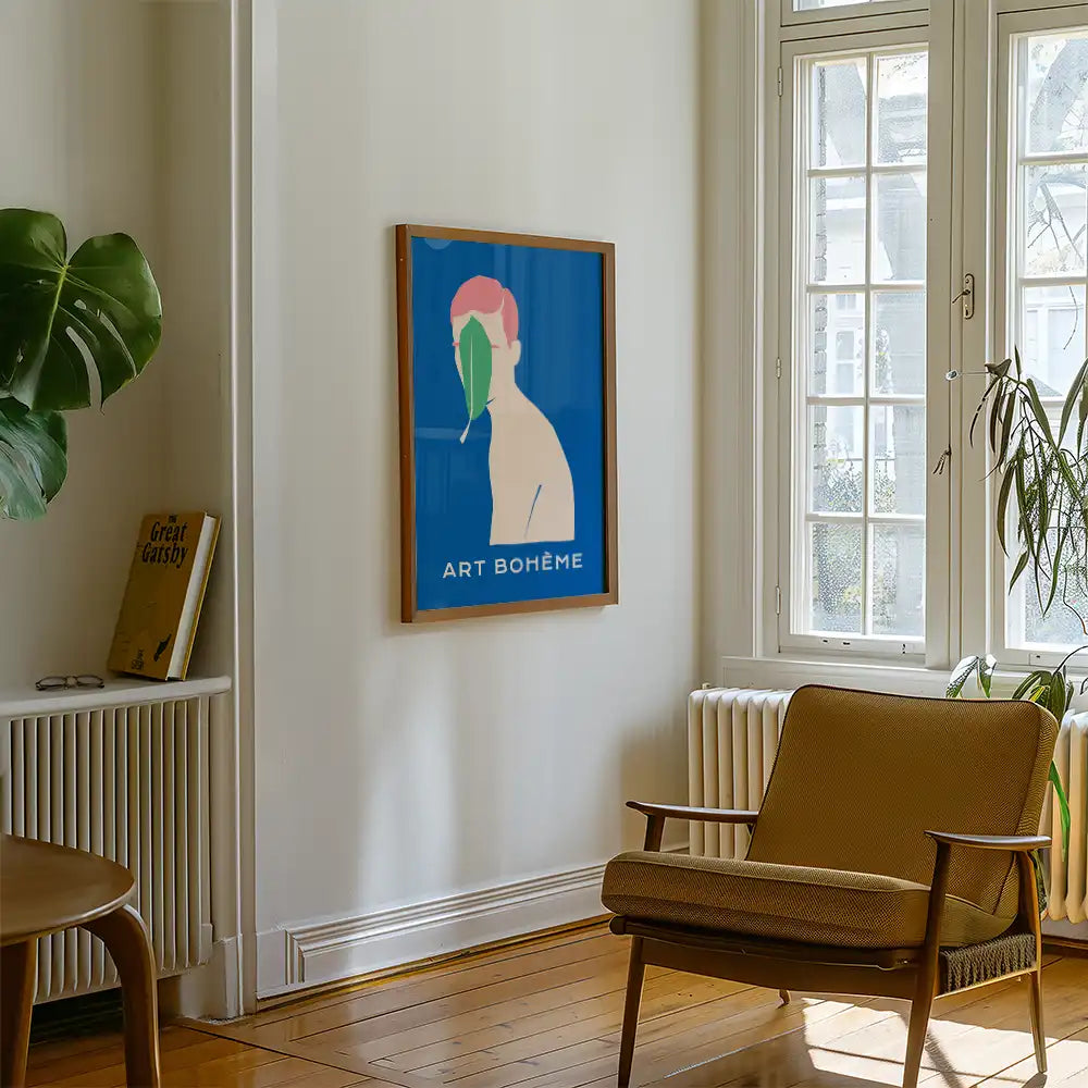 Modern poster reprint of a famous painting featuring a colorful figure with a leaf on a blue background, titled "ART BOHÈME," displayed in a stylish interior setting with a cozy chair and greenery.