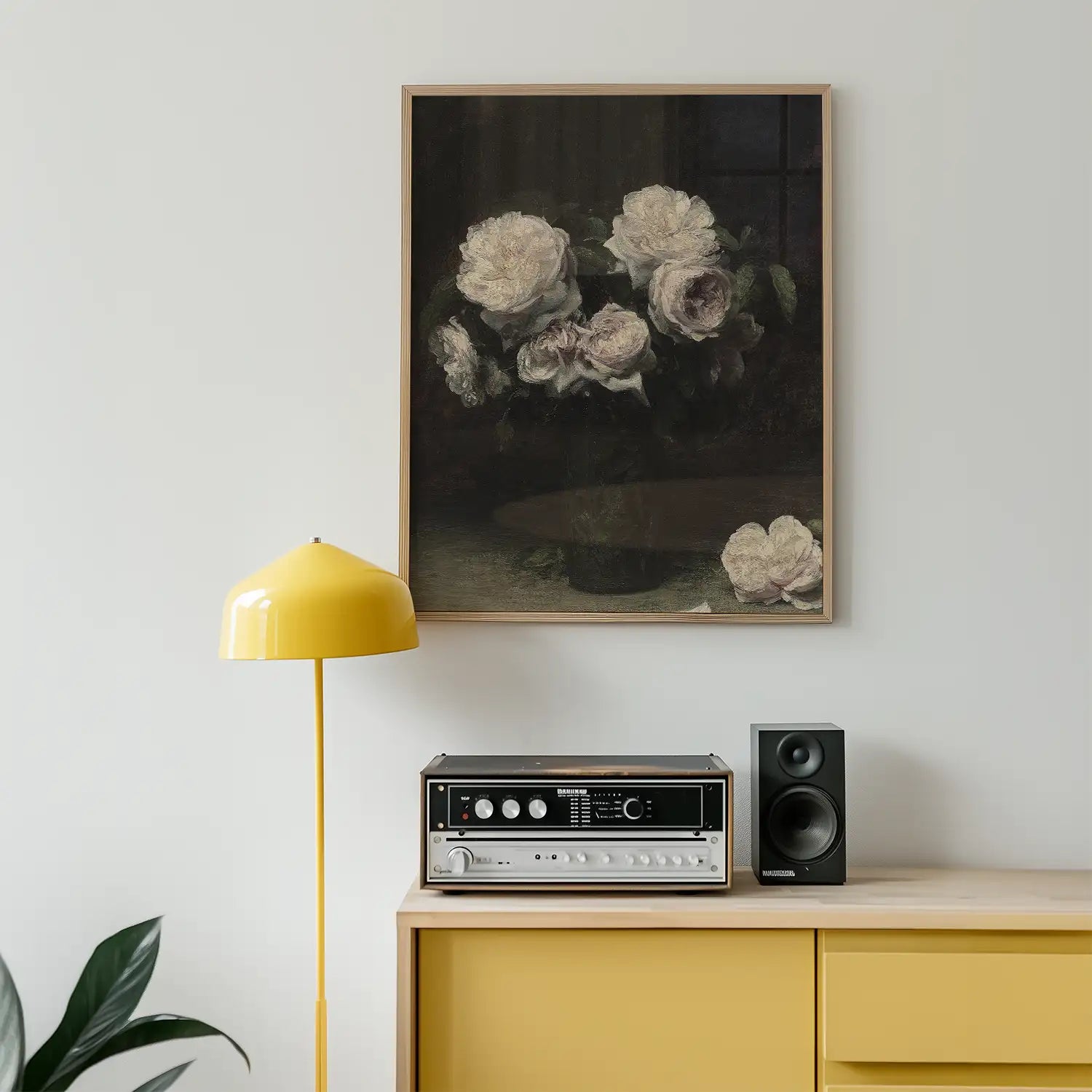 A vintage-style painting of white and light pink roses in a vase, framed and displayed on a wall above a wooden sideboard with a yellow lamp and a vintage audio system.
