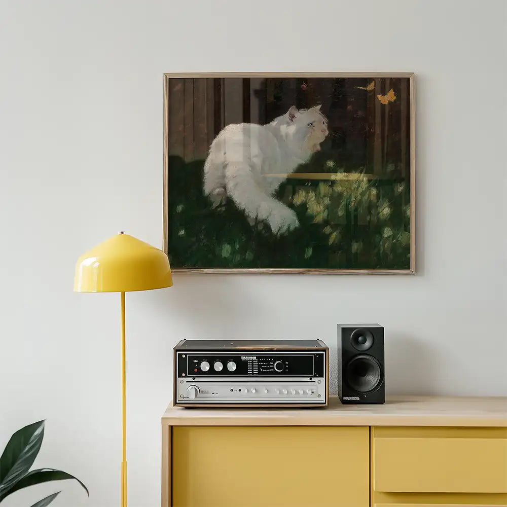Painting of a white cat lounging and looking at butterflies, framed, displayed above a retro stereo system and yellow lamp in a modern living space.