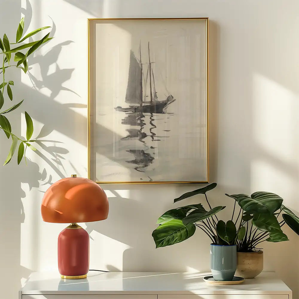 Artistic painting of a sailboat reflected on water, framed in gold, displayed in a bright room with a colorful lamp and potted plants.