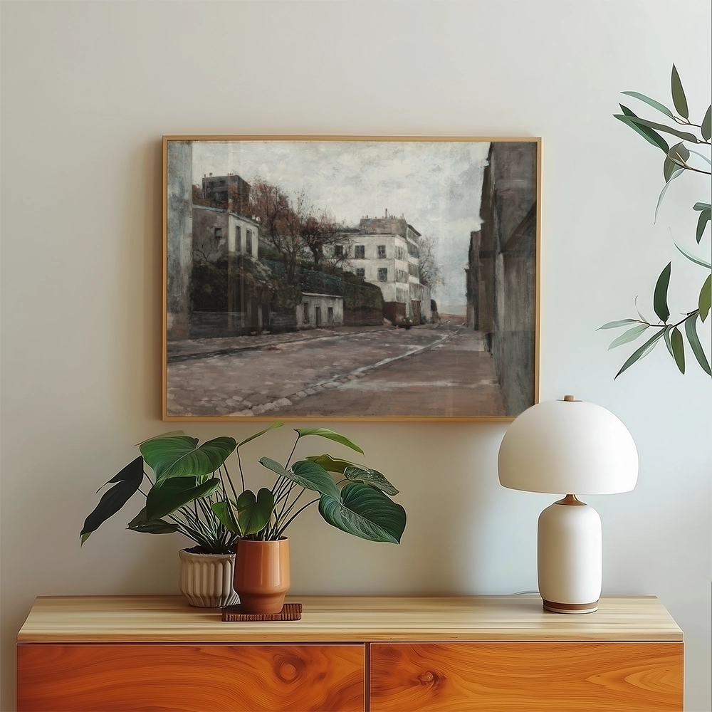 A vintage street scene painting framed in wood, displayed above a modern wooden sideboard with plants and a lamp.