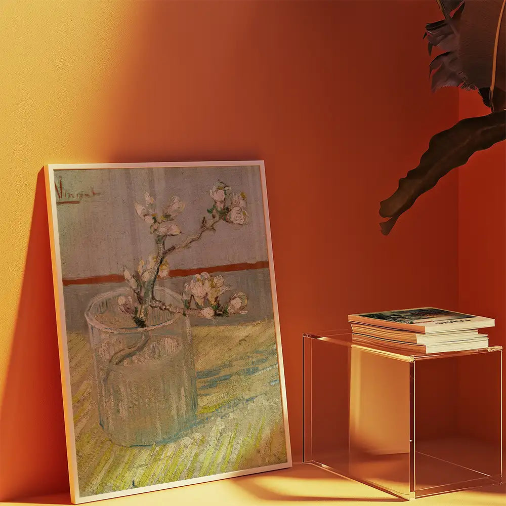Painting of a flowering branch in a glass vase displayed against an orange wall, with a clear side table holding stacked books.