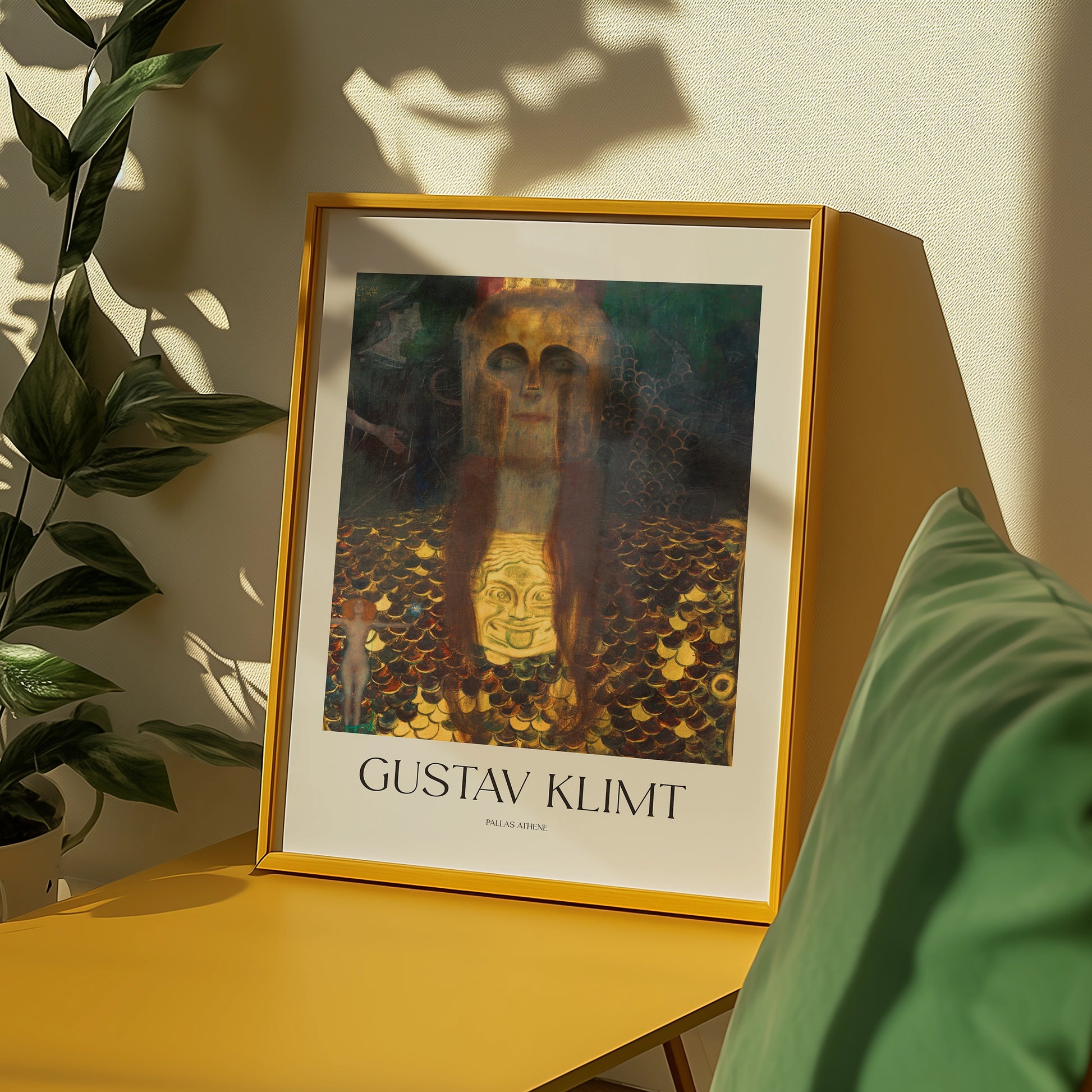 Framed painting by Gustav Klimt featuring abstract figures, displayed on a yellow table with green cushions and plants in the background.