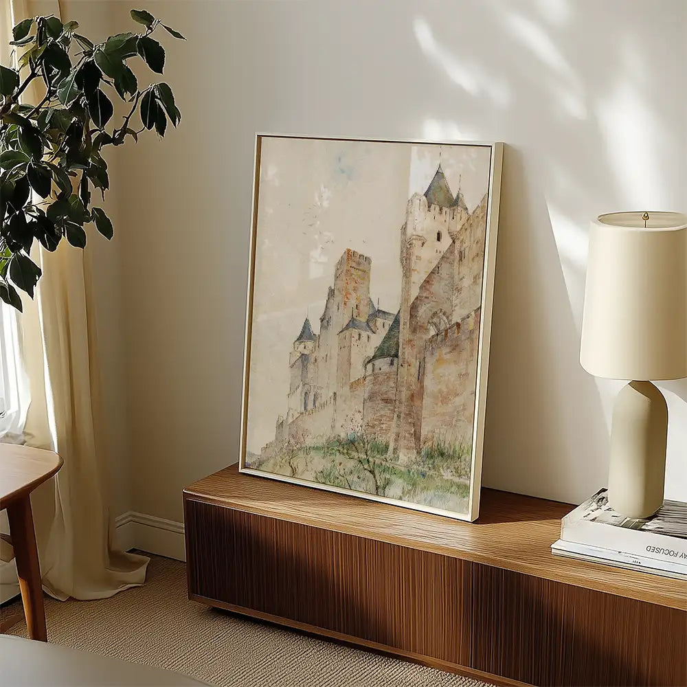Framed painting of a medieval castle displayed on a wooden side table next to a lamp and a plant.