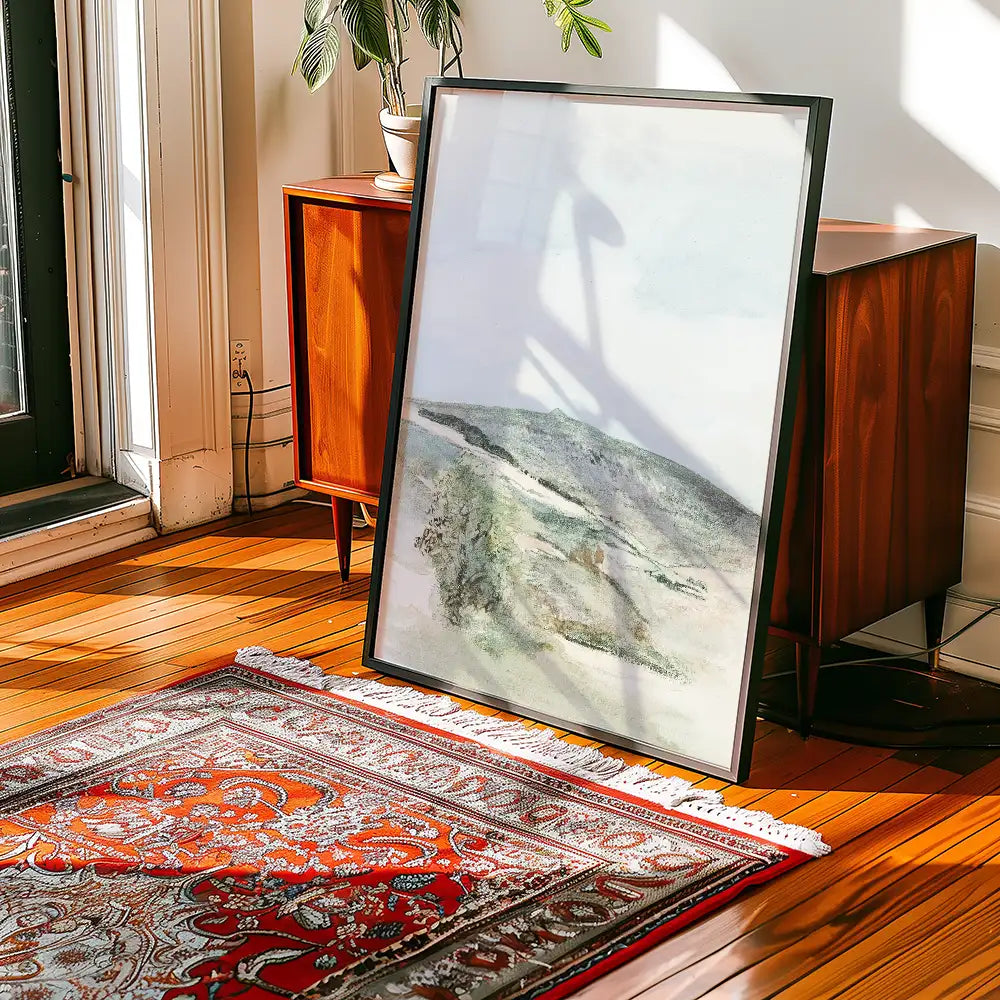 Framed abstract landscape painting leaning against a mid-century modern cabinet on a wooden floor with a patterned area rug.