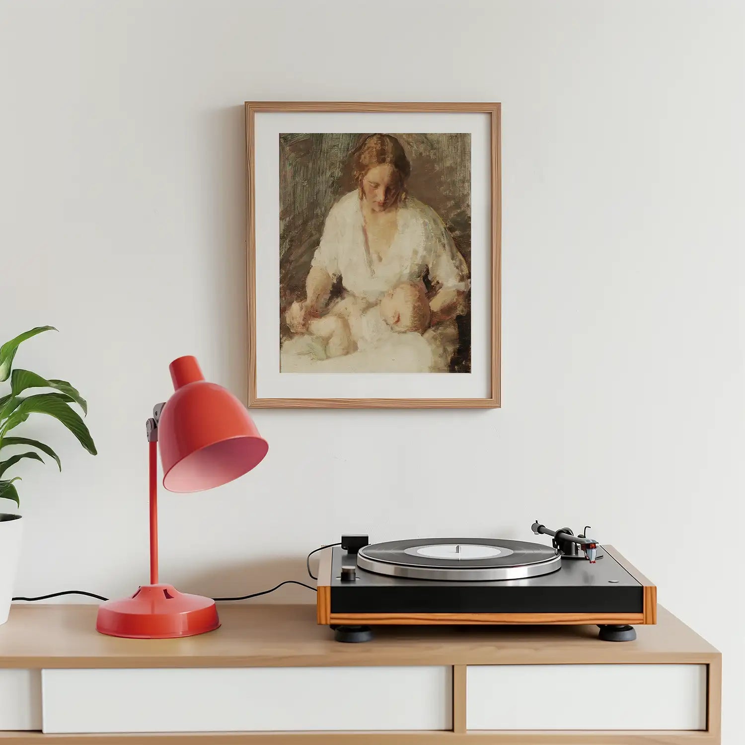 Framed painting of a woman with a child, displayed on a wall above a wooden table with a red desk lamp and a vinyl record player.