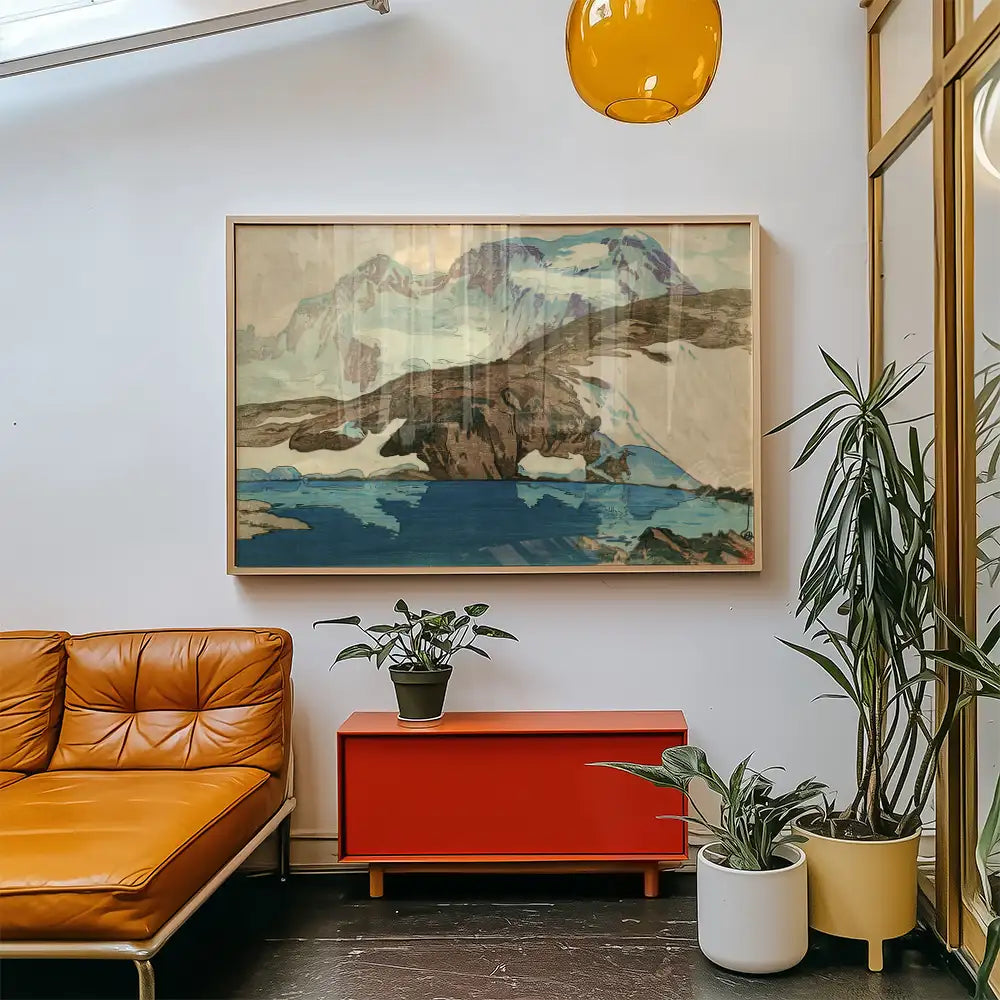 Framed landscape painting featuring mountains and a lake, displayed in a contemporary living room setting with a leather sofa and indoor plants.
