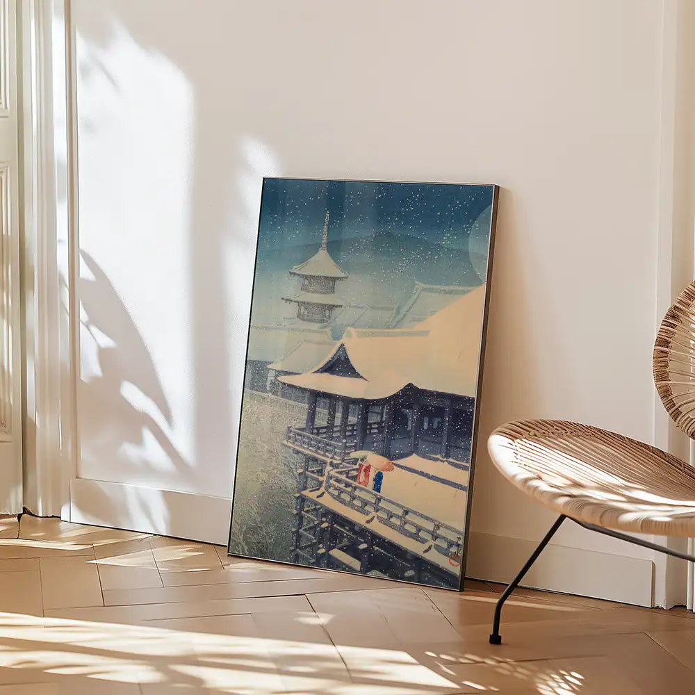 Painting of a serene winter scene featuring a traditional Japanese building, framed and leaning against a wall, with light shadows and a modern chair in the foreground.