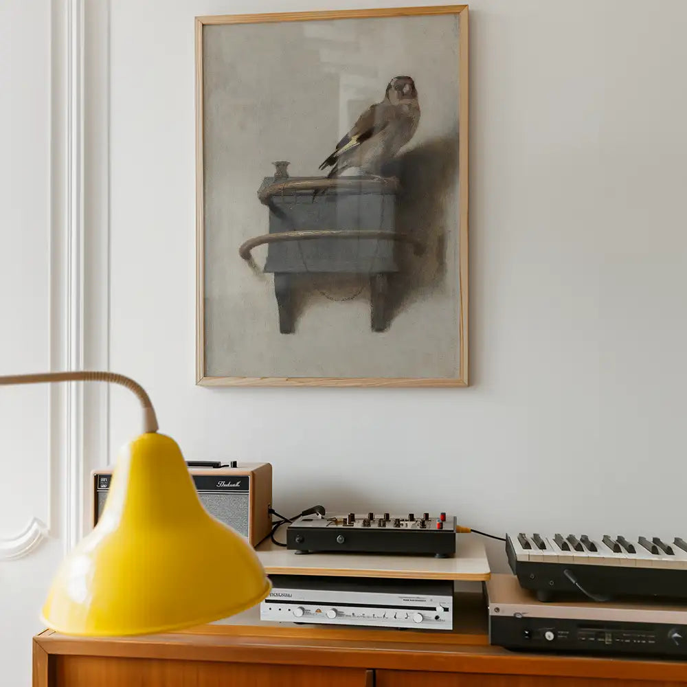 A framed painting of a bird perched on a grey box, displayed on a wall above a wooden console with vintage audio equipment and a yellow pendant lamp.