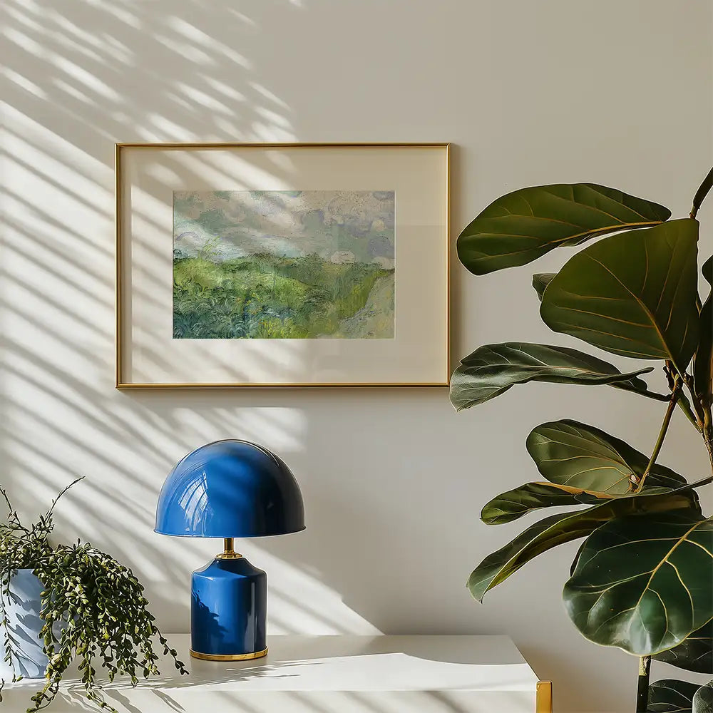Framed landscape painting in soft greens and blues on a wall, accompanied by a blue lamp and indoor plant.
