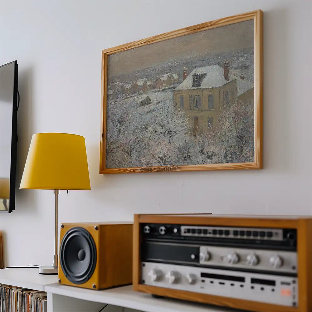 Framed painting of a winter scene featuring a house surrounded by snow, displayed on a white wall next to a yellow lamp and vintage audio equipment.