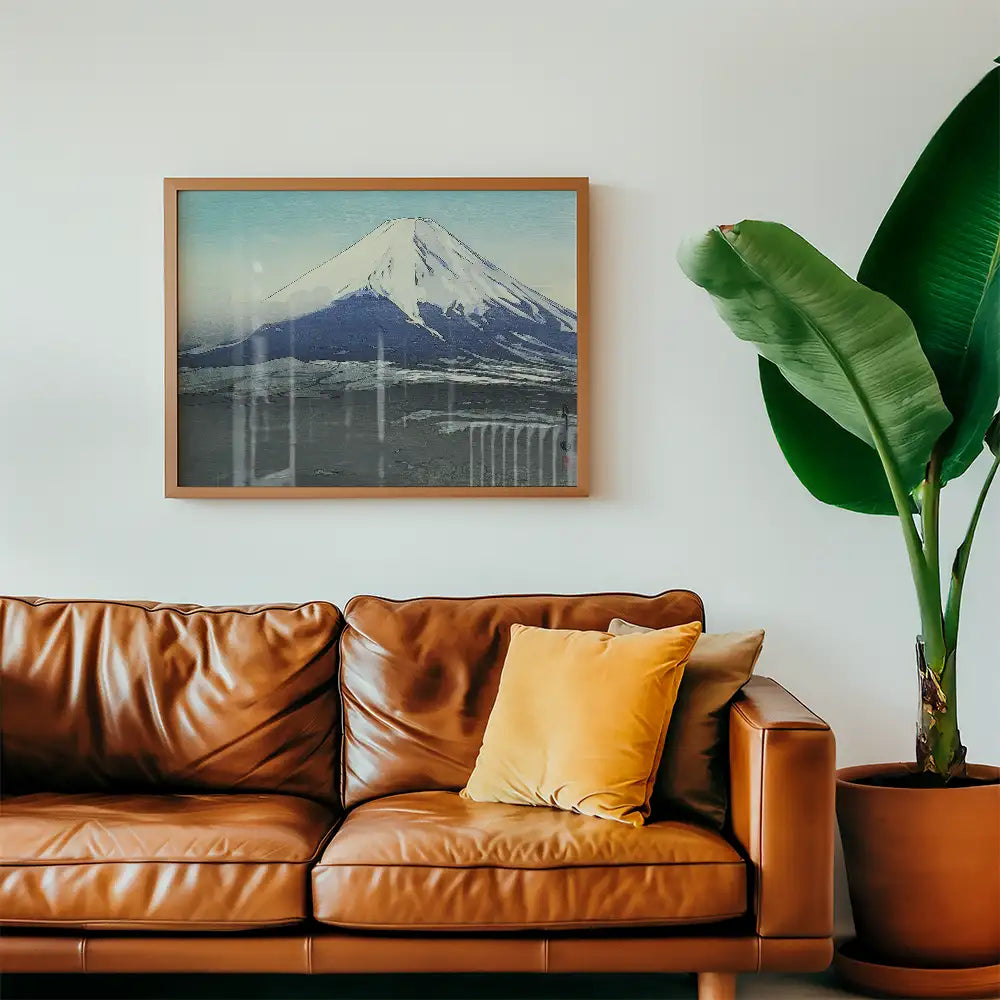 Framed painting of Mount Fuji above a brown leather sofa with a yellow cushion and a green plant.