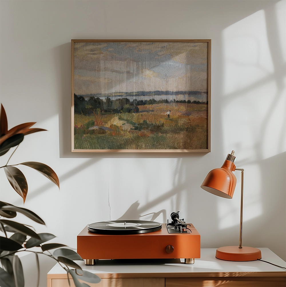 Painting of a landscape with fields and a lake, framed above a vintage record player and an orange desk lamp in a bright, modern interior setting.