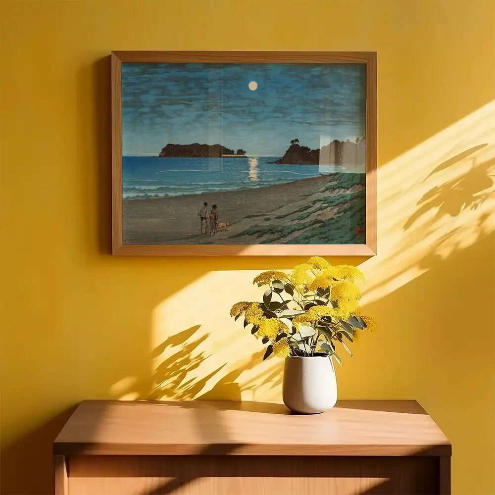 Framed painting of a serene beach scene with two figures and a dog, displayed on a yellow wall above a wooden table with a vase of yellow flowers.
