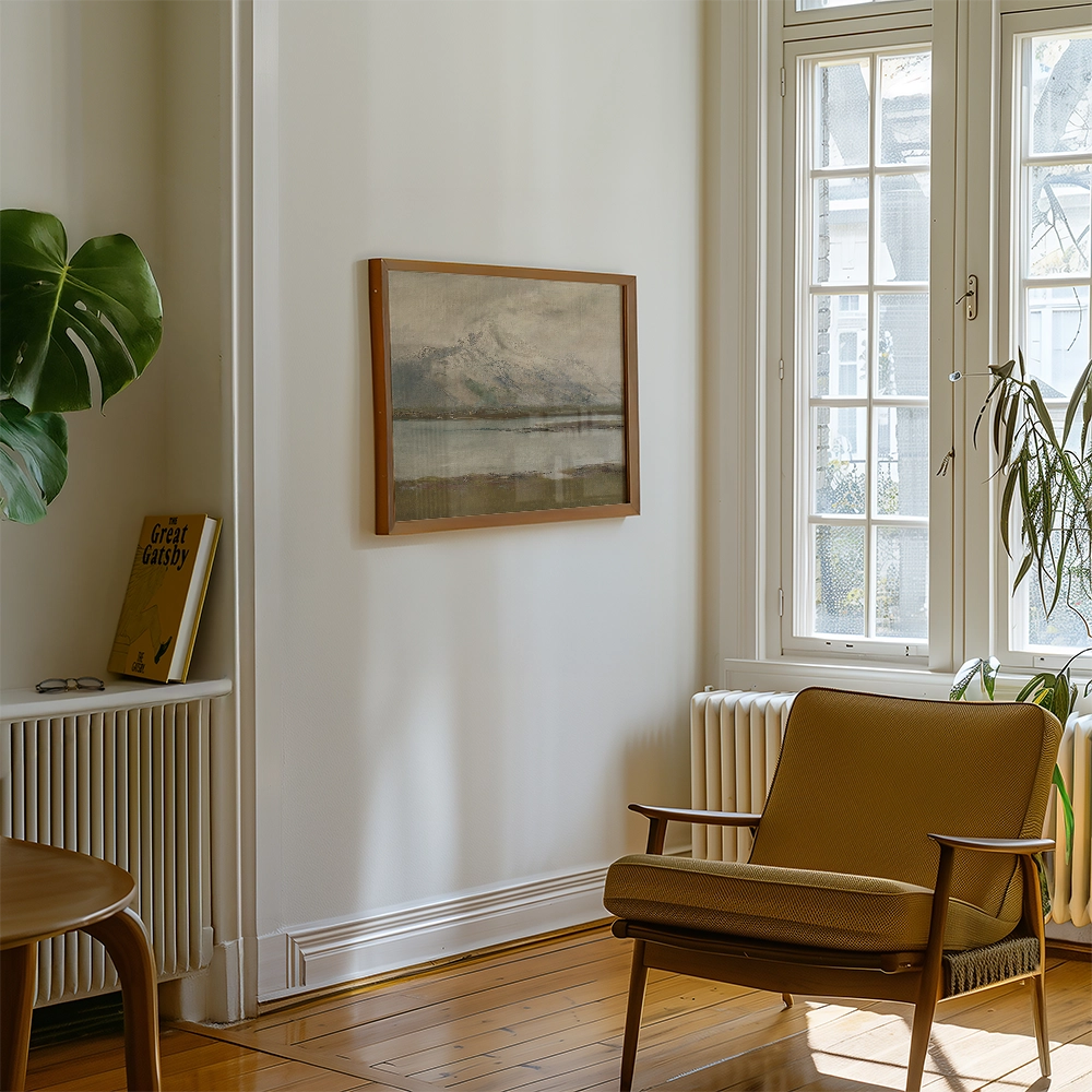 Framed landscape painting on a wall in a modern living room with a wooden chair and green plant.
