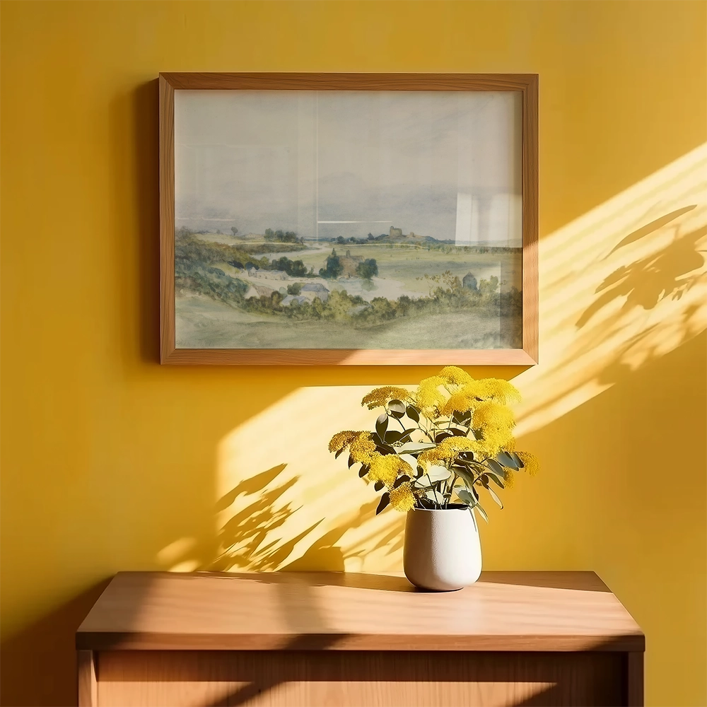 Framed landscape painting above a wooden dresser with a vase of yellow flowers on top, set against a vibrant yellow wall.
