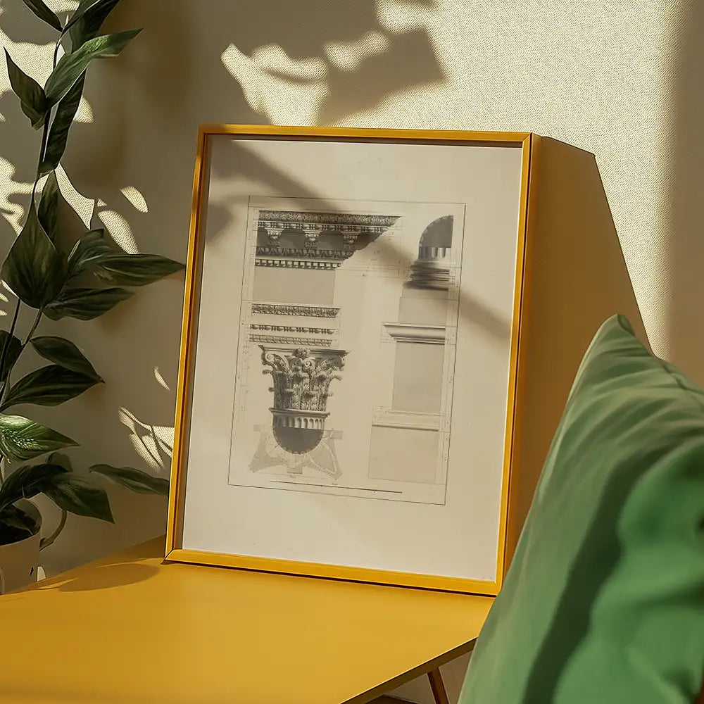 Framed architectural drawing of a decorative column displayed on a yellow table, with a green pillow and plant in the background.