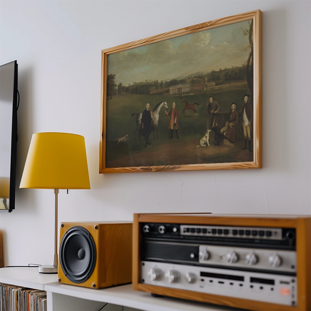 Painting of horsemen and dogs in a countryside scene, framed and displayed on a wall next to a yellow lamp and vintage audio equipment.
