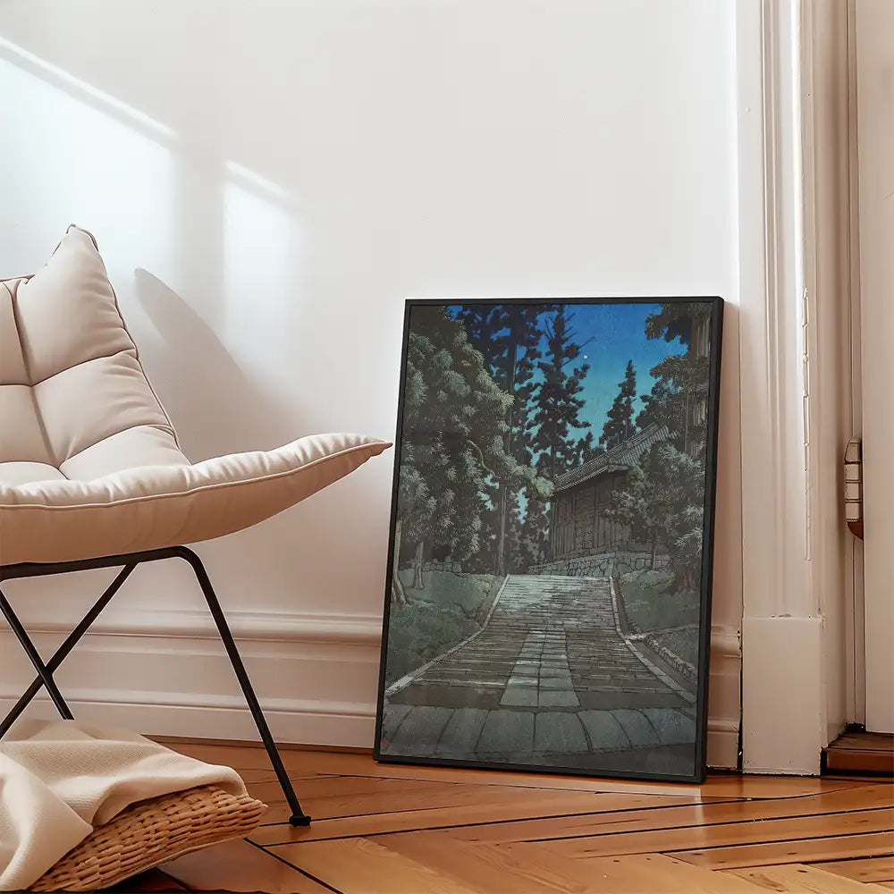 Framed painting of a serene pathway lined with trees, leaning against a wall next to a modern chair in a bright, airy room.