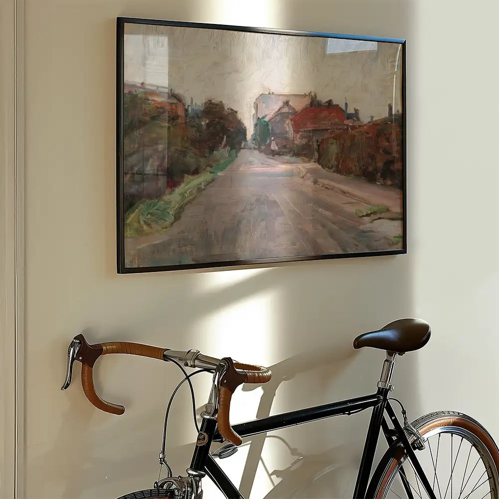 Framed painting of a scenic road and houses hanging on a wall next to a bicycle with brown handlebars.