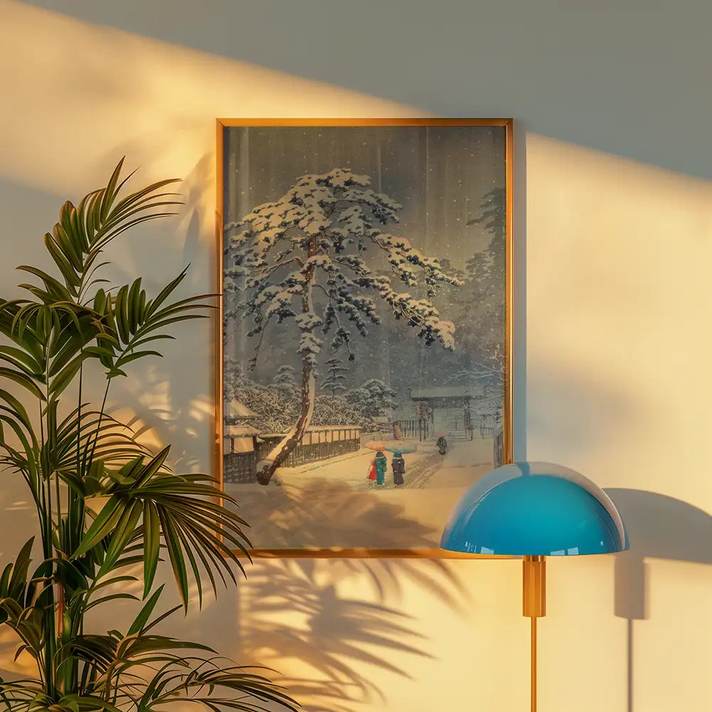A winter landscape painting framed in gold, depicting snowy trees and two figures in winter attire, alongside a green plant and a blue lamp.