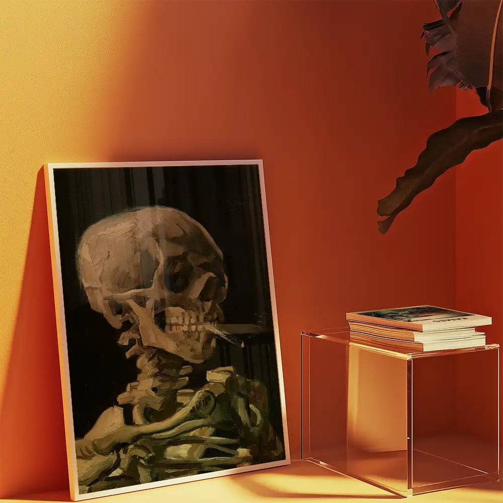 Framed painting of a skeleton with a cigarette, placed beside a stack of books on a transparent acrylic table against an orange wall.