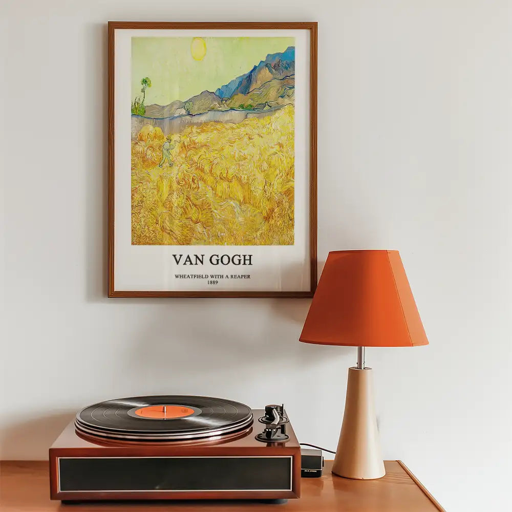Poster of Van Gogh's "Wheatfield with a Reaper" framed and displayed on a wall above a record player and a modern orange lampshade.