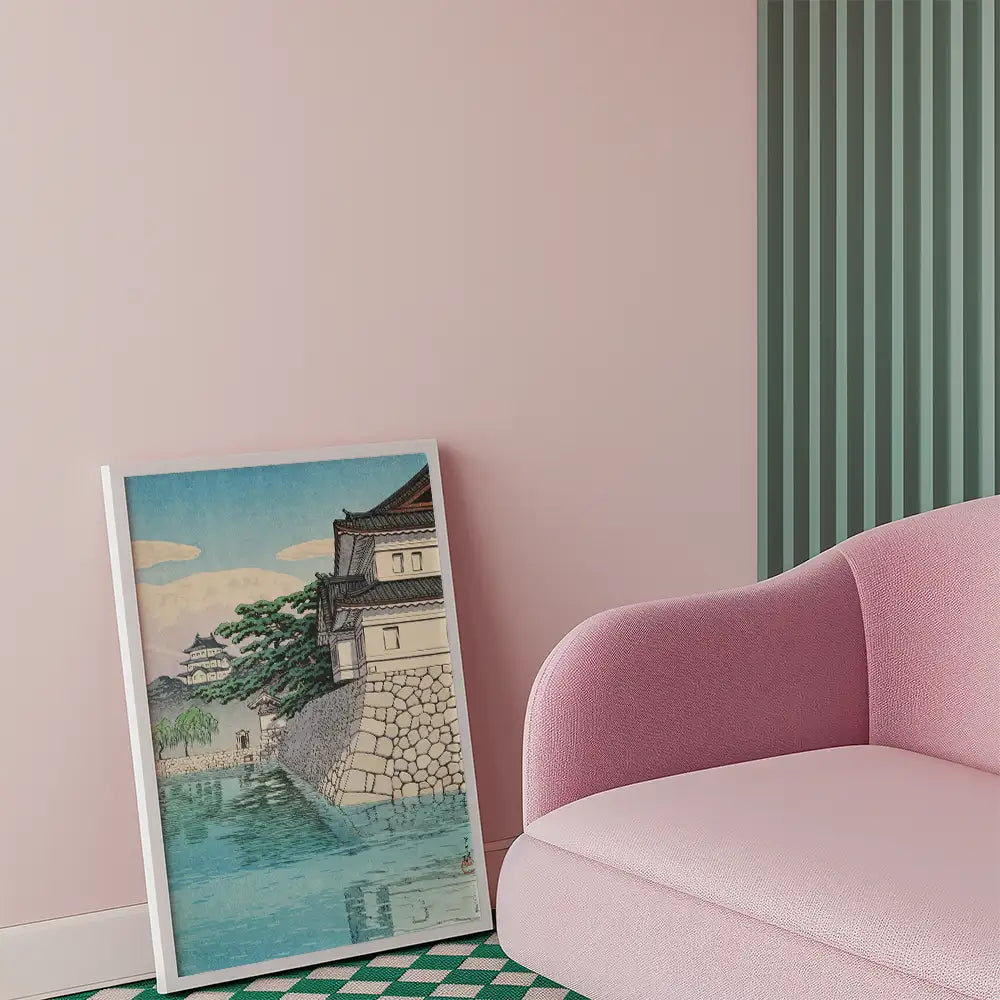Painting of a traditional Japanese landscape featuring a castle by a river, displayed in a modern interior with a pink couch.