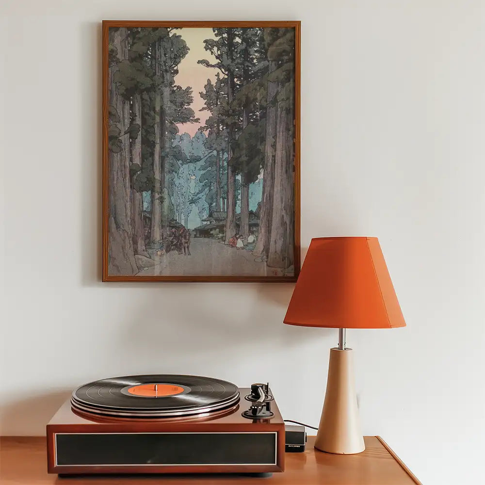 Framed painting of a tranquil forest scene with tall trees and a pathway, displayed above a vintage record player and an orange lamp.