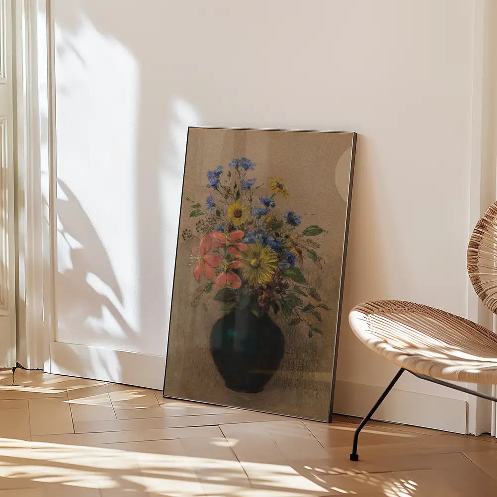 Framed painting of colorful flowers in a vase leaning against a wall in a sunlit room with wooden flooring and a modern chair.