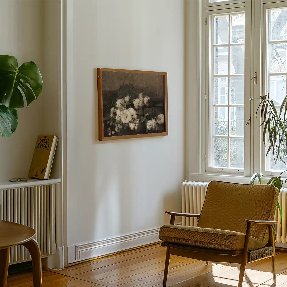 Framed floral painting on a wall in a cozy living room with a chair and a bookshelf.