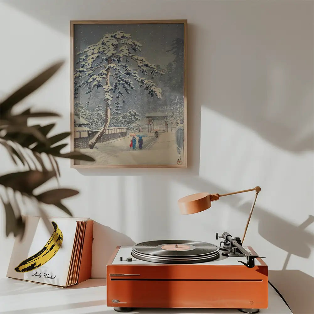 Winter landscape painting hanging above a retro record player with an orange base and a lamp in a cozy room setting.