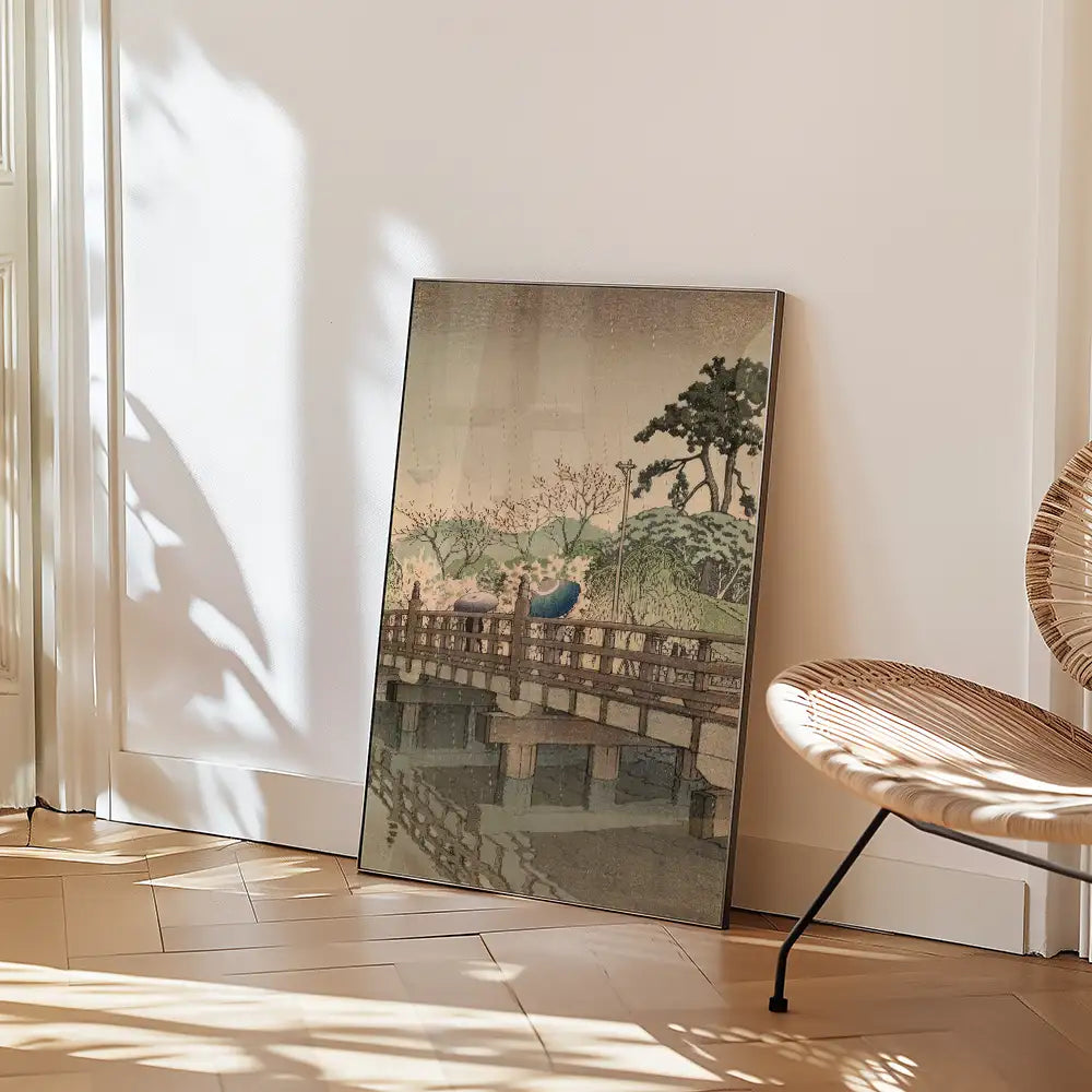Painting of a serene landscape with a bridge and trees, leaning against a wall beside a stylish chair in a bright room.