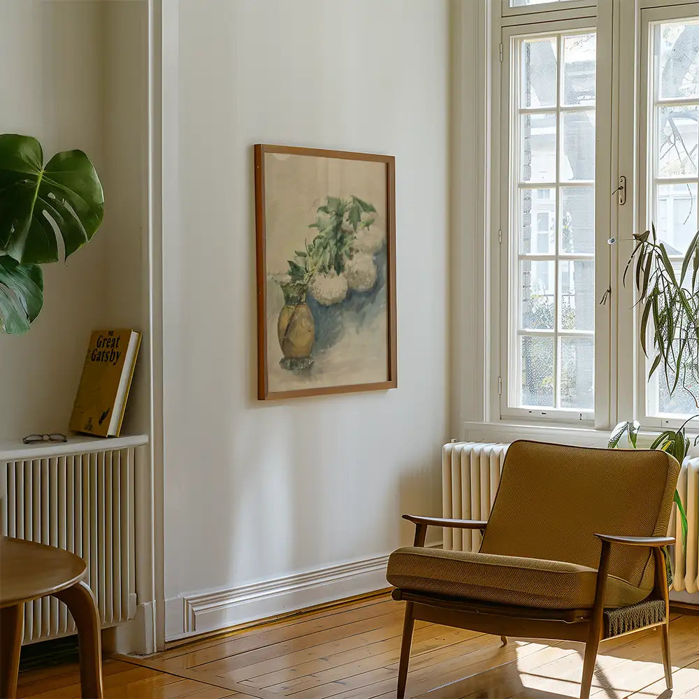 A framed painting of a vase with white flowers hanging on a wall in a cozy living room setting with a wooden chair and a potted plant.